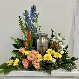 Floral urn arrangement with blue delphinium, tulips, roses, and yellow daisies