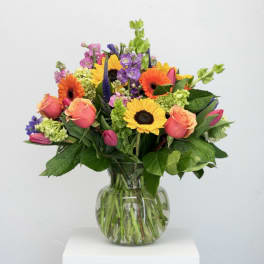 Mixed bouquet of sunflowers, roses, and purple flowers in a glass vase