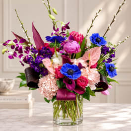 Colorful mixed bouquet in a clear glass vase with blue, pink, and purple blooms