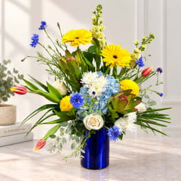 Mixed bouquet in a blue vase with yellow, white, blue, and pink flowers