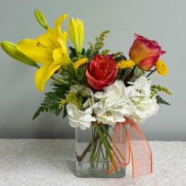 Yellow lilies and red roses in a clear glass vase with white hydrangeas