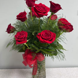 Red roses arranged in a clear glass vase with a red ribbon