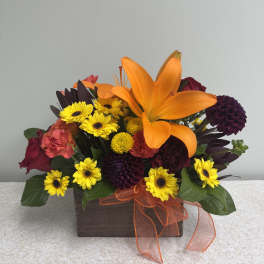 Orange lily and mixed yellow and burgundy flowers in a wooden box