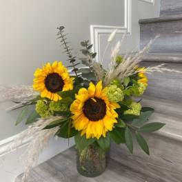 Sunflower arrangement in a glass vase with green accents and dried grasses