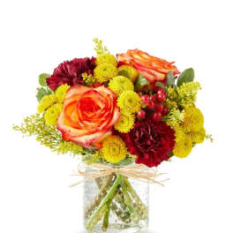 Bouquet of orange roses and yellow and burgundy flowers in a glass vase