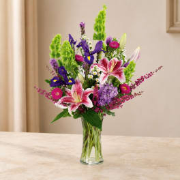Mixed bouquet of lilies, irises, and purple flowers in a clear glass vase