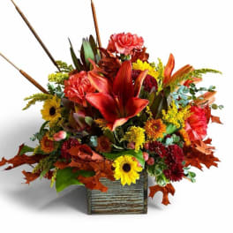 Autumn floral arrangement with red lilies and yellow sunflowers in a rustic wooden container