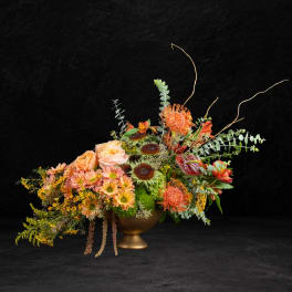 Orange and peach floral arrangement in a gold pedestal vase