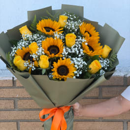 Bouquet of sunflowers and yellow roses wrapped in olive paper with an orange ribbon