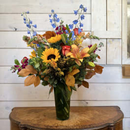 Mixed bouquet with sunflowers, lilies, and blue delphinium in a tall vase