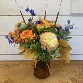 Mixed bouquet in a brown glass vase with orange roses and blue flowers