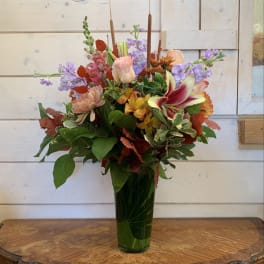 Mixed bouquet in a tall green glass vase with pink and purple blooms