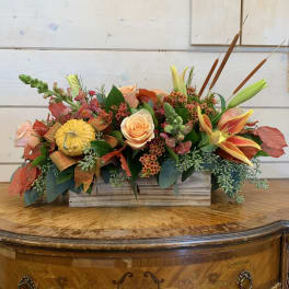 Autumn floral arrangement in a wooden box with roses, lilies, and a small pumpkin