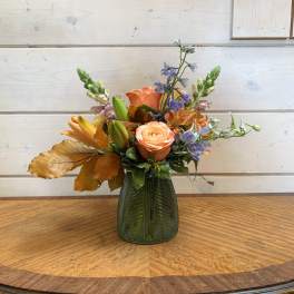 Peach and blue mixed flower arrangement in a green glass vase