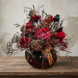 Red roses in a dark vase with dried accents and seed pods