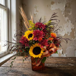 Sunflower and burgundy mum arrangement in an amber vase with plaid ribbon