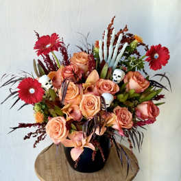 Peach roses and red gerbera daisies in a black vase with skull accents