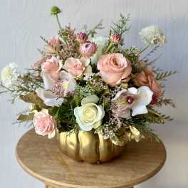 Pink and white floral arrangement in a gold pumpkin vase