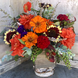 Bright mixed bouquet with orange, red, and purple flowers in a rustic wooden container