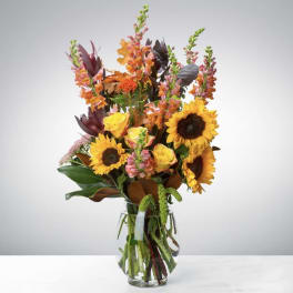 Tall bouquet of sunflowers, roses, and snapdragons in a glass vase