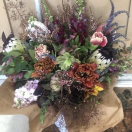 Large mixed bouquet with purple, pink, white, and orange blooms wrapped in brown paper