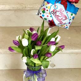 Purple and white tulips in a glass vase with a birthday balloon