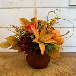 Fall floral arrangement in a pumpkin-shaped container with orange lilies and roses