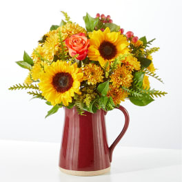 Sunflowers and orange roses arranged in a red pitcher vase