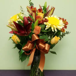 Mixed bouquet of lilies, roses, and daisies in a glass vase with a ribbon