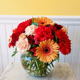 Mixed red, peach, and orange flowers arranged in a glass bowl vase