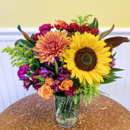 Mixed bouquet in a clear glass vase with a large sunflower and orange blooms