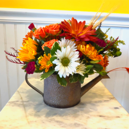 Mixed orange, white, and yellow flowers arranged in a metal watering can