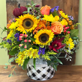 Mixed bouquet with sunflowers, roses, and colorful filler flowers in a patterned vase