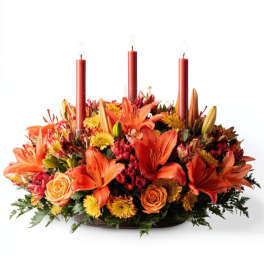 Low floral centerpiece with orange lilies, roses, and three red taper candles