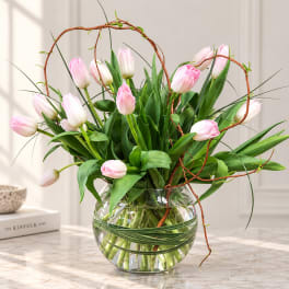 Pink tulips arranged in a clear glass bowl vase with curly branches