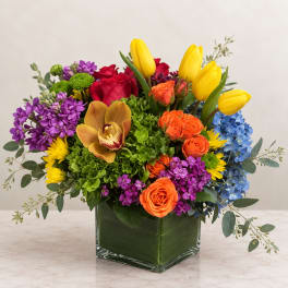 Colorful mixed bouquet in a square glass vase with tulips, roses, orchids, and hydrangeas