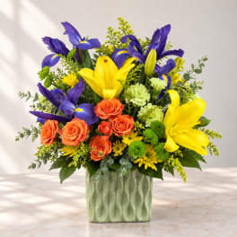 Bright bouquet of yellow lilies, purple irises, and orange roses in a green vase