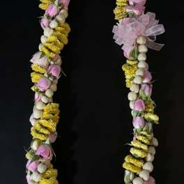 Floral lei with pink buds, yellow flowers, and white beads on a black background
