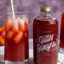 Glass of red drink with ice beside a glitter sangria bottle