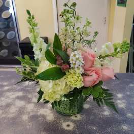 Pink roses and white flowers arranged in a green glass vase