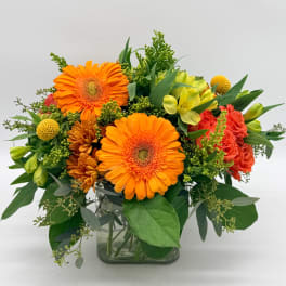 Bright mixed flower arrangement in a clear glass vase with orange gerberas and coral blooms
