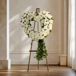 White rose heart wreath on a stand with trailing greenery