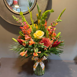 Mixed bouquet in a glass vase with yellow roses, lilies, and orange blooms