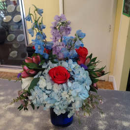 Blue and lavender floral arrangement with red roses in a blue vase