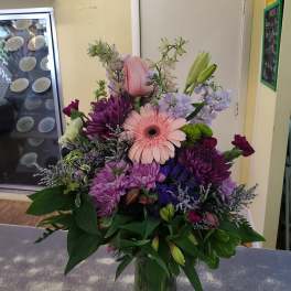 Mixed bouquet with pink gerbera daisy, purple chrysanthemums, and lilies in a glass vase