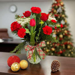 Red carnations and tulips in a glass vase with plaid bow, with ornaments and a pinecone on the table.