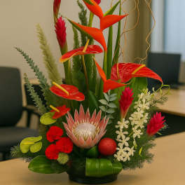 Tall tropical arrangement with red, orange, and white flowers in a low black container on a table