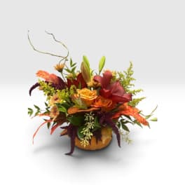 Autumn floral arrangement in a pumpkin-shaped container with orange and red blooms