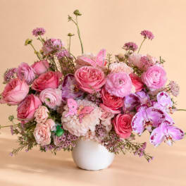Pink mixed flower arrangement in a white vase with butterfly picks