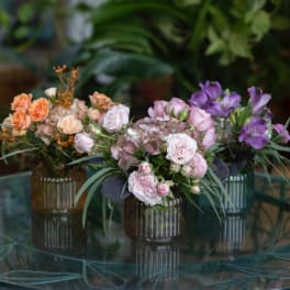 Three small floral arrangements in ribbed glass vases on a table